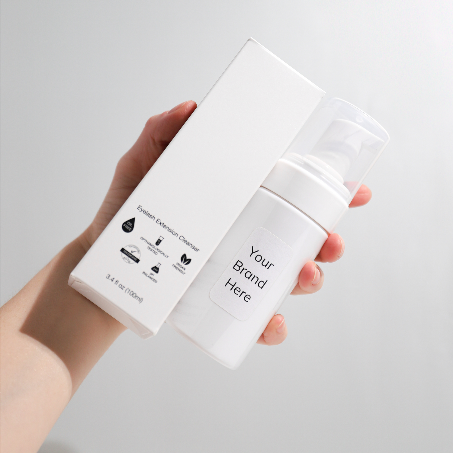 Hand holding a white bottle and box with 'Your Brand Here' text on a light gray background
