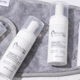 Flat lay of Prolong Lash cleanser bottles and tools on a white tiled surface with a grey towel.