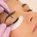 Gloved lash technician inspecting extensions with tweezers.