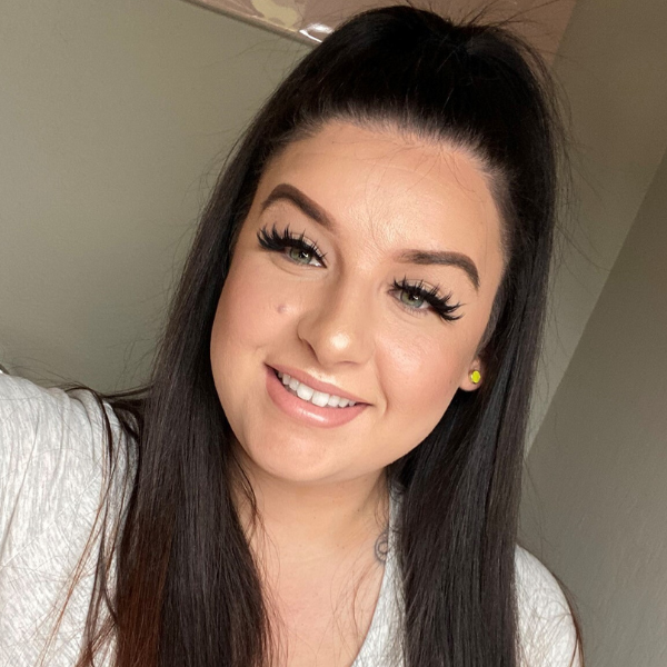 Woman with long dark hair and makeup smiling indoors.