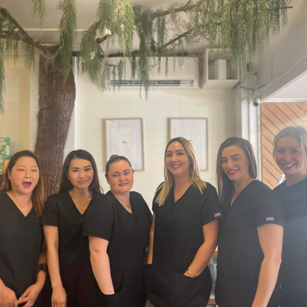 Group of six women in black uniforms posing together in a room with plants and framed pictures on the wall.