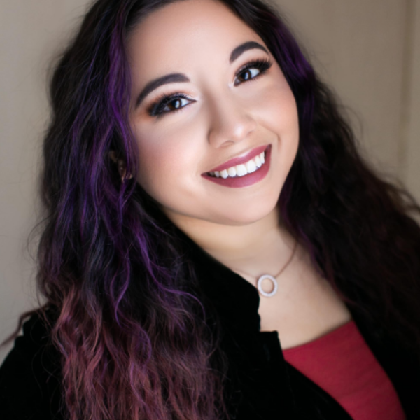 Woman with purple hair smiling against a neutral background