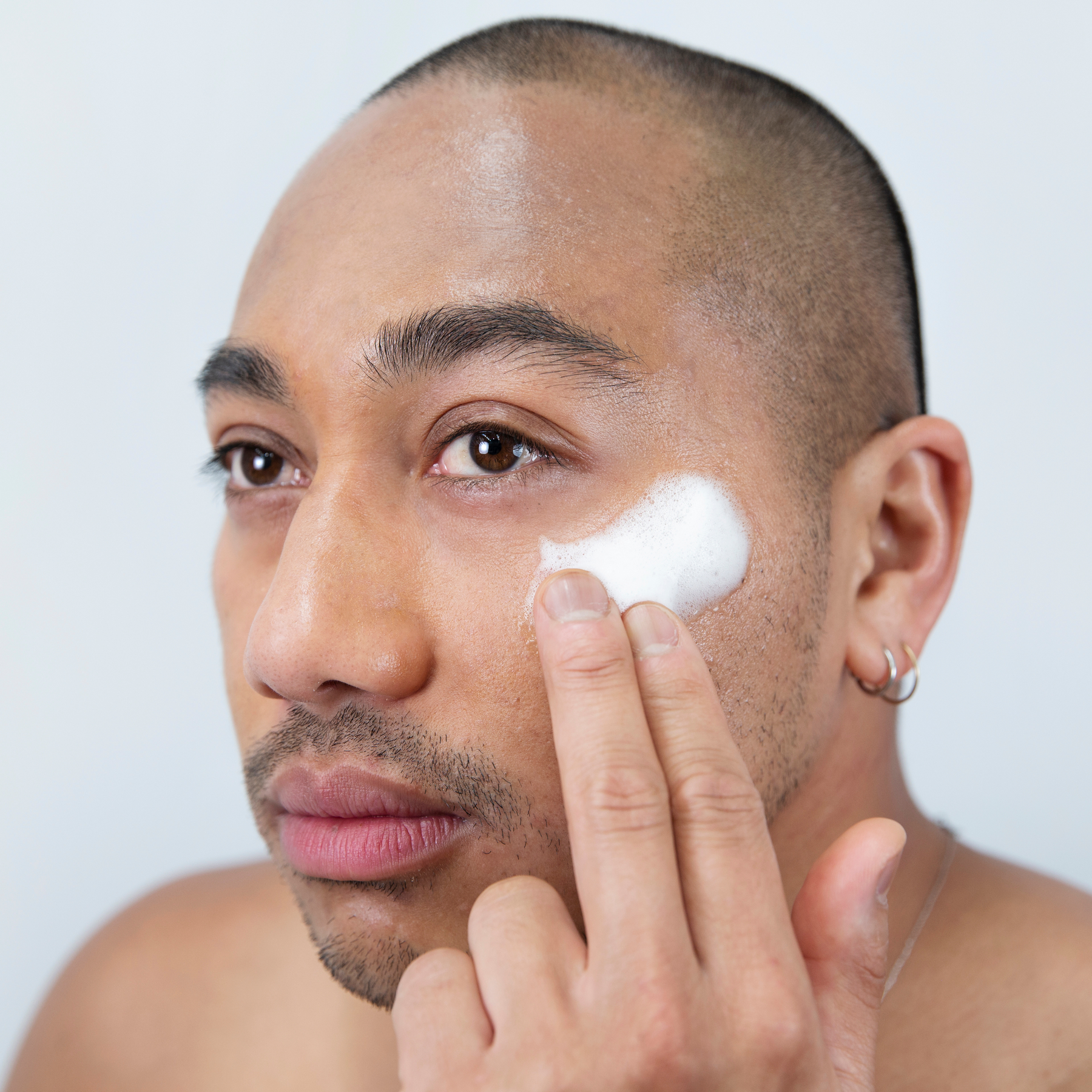 Man applying foaming cleanser to his face with a neutral background