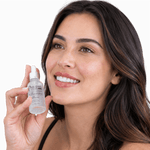 A smiling woman with long dark brown hair holds a small clear dropper bottle of Prolong Lash oil-free hydrating serum against a clean white background.