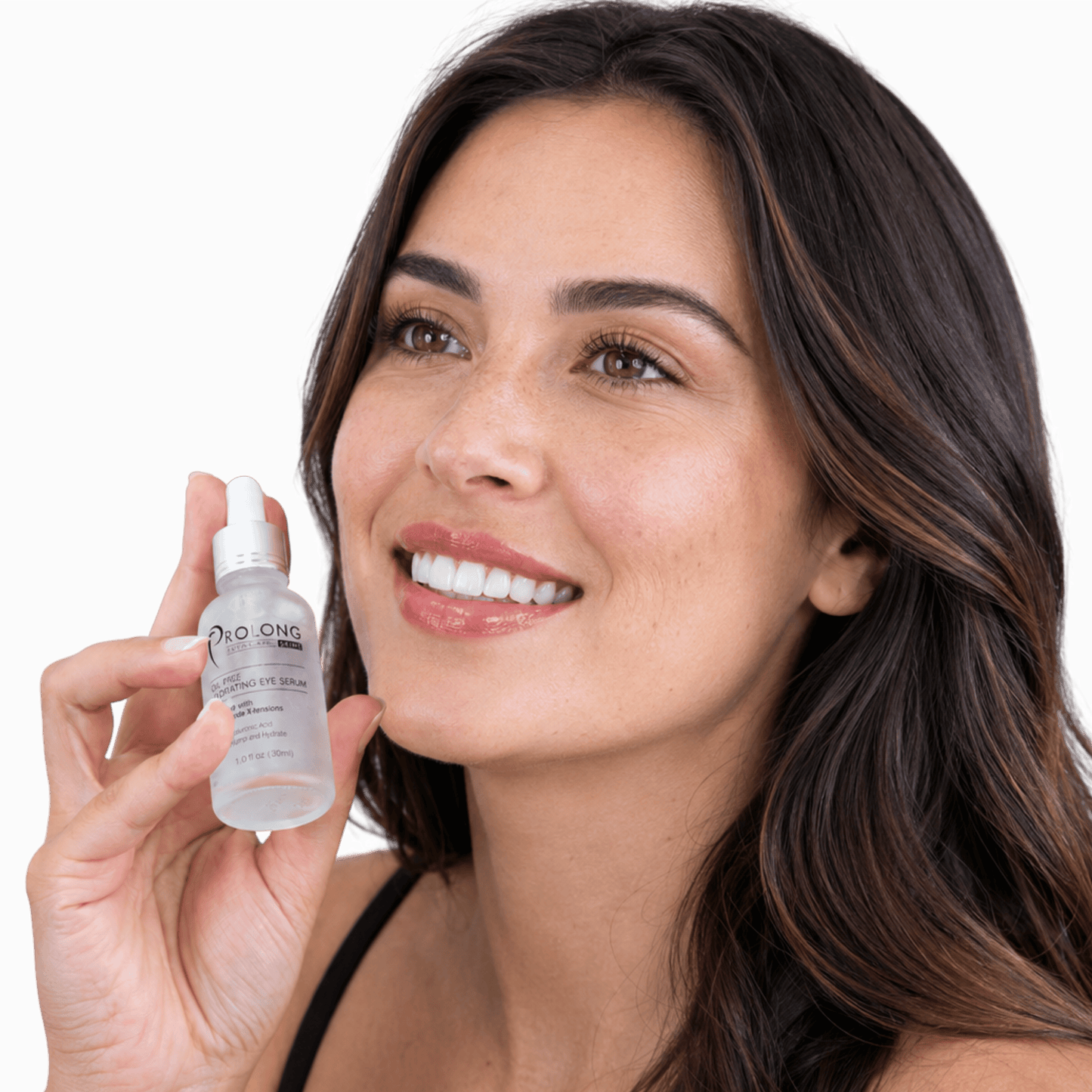 A smiling woman with long dark brown hair holds a small clear dropper bottle of Prolong Lash oil-free hydrating serum against a clean white background.