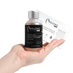 A hand holds a small bottle of Prolong Lash Complete Care Eyelash Extension Cleanser and Daily Face Cleanser Concentrate next to a prolong lash retail label on a solid white background.