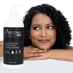 A bottle of Prolong Professional eyelash extensions and daily facial cleaner concentrate shown in front of a smiling woman with dark curly hair resting her head on her hands against a clean white background.
