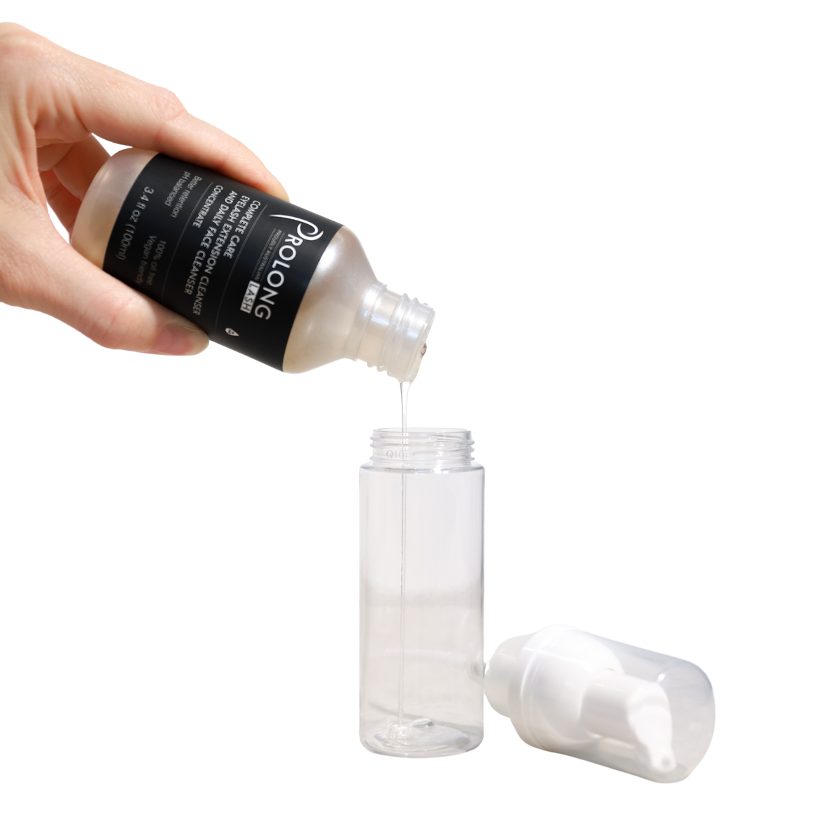A hand pours prolong lash concentrate from a black-labeled bottle into a clear cylindrical pump bottle, with the white pump cap placed beside it on a white background.