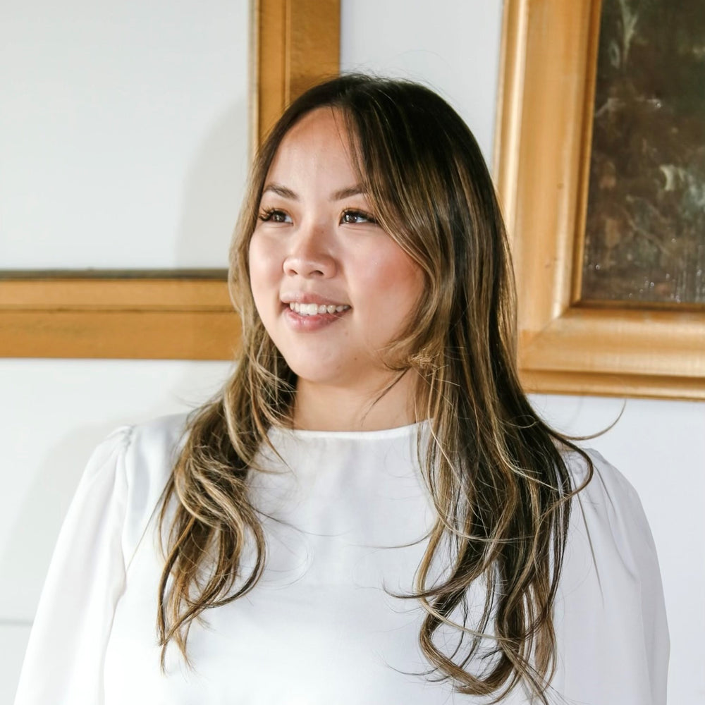 Woman with long hair wearing a white shirt in front of framed pictures.